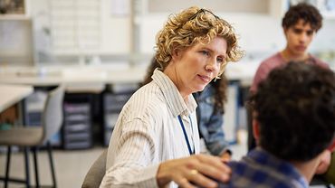 Eine Frau legt einem jungen Mann eine Hand auf die Schulter und blickt ihn mit ermutigendem Blick an