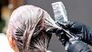 Friseurin oder Friseur beim Auftragen von Farbe auf den Kopf einer Kundin. Die Friseurin oder der Friseur trägt schwarze Handschuhe mit Farbspuren und hält einen Kamm in der Hand