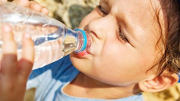 Schwitzendes Kleinkind, das aus einer Wasserflasche trinkt