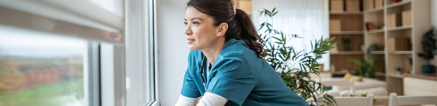 Eine Krankenschwester macht eine Pause und schaut aus dem Fenster.