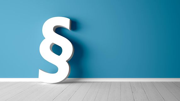 Ein Paragraphen-Modell lehnt an einer blauen Wand