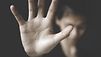 Eine zur Abwehr nach vorn gestreckte Hand im Vordergrund. Hinten verschwommen eine Frau mit gesenktem Kopf.