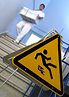Eine Krankenpflegerin in weißer Berufskleidung geht eine Treppe hinunter. Danei trägt sie eine große Gitterbox mit gefalteter, weißer Wäsche. Im Vordergrund ein gelbes, dreieckiges Warnschild mit dem Symbol "Vorsicht Rutschgefahr"