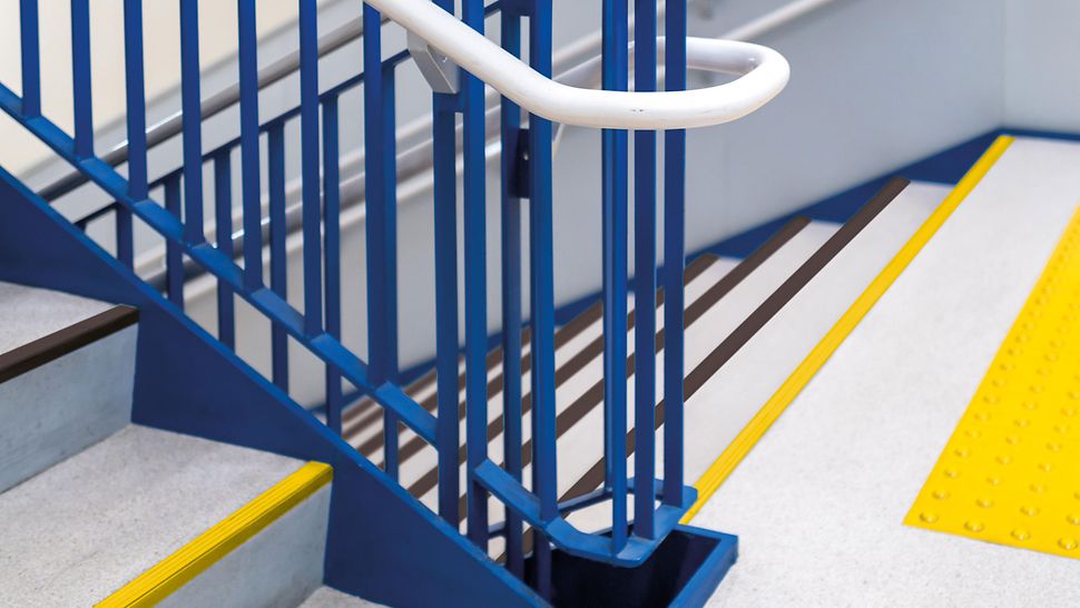 Treppe im Treppenhaus mit Handlauf und taktilen Streifen.