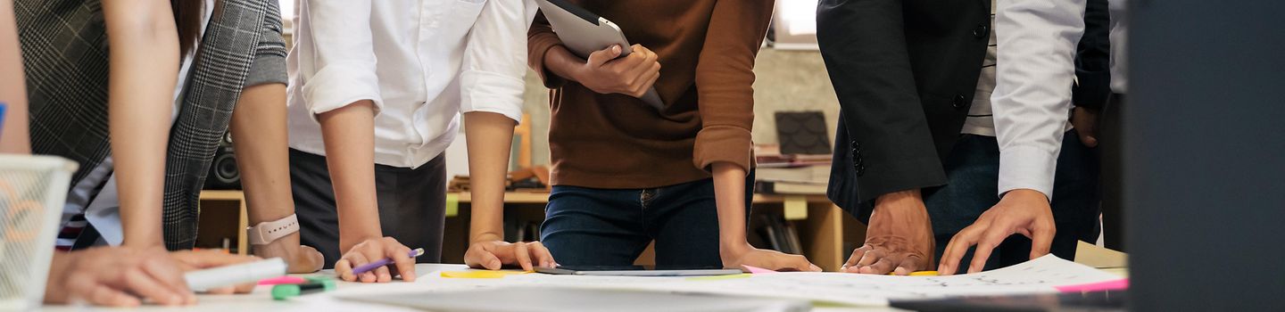 Eine Gruppe Menschen steht um einen Tisch mit Zetteln und Stiften und bespricht sich