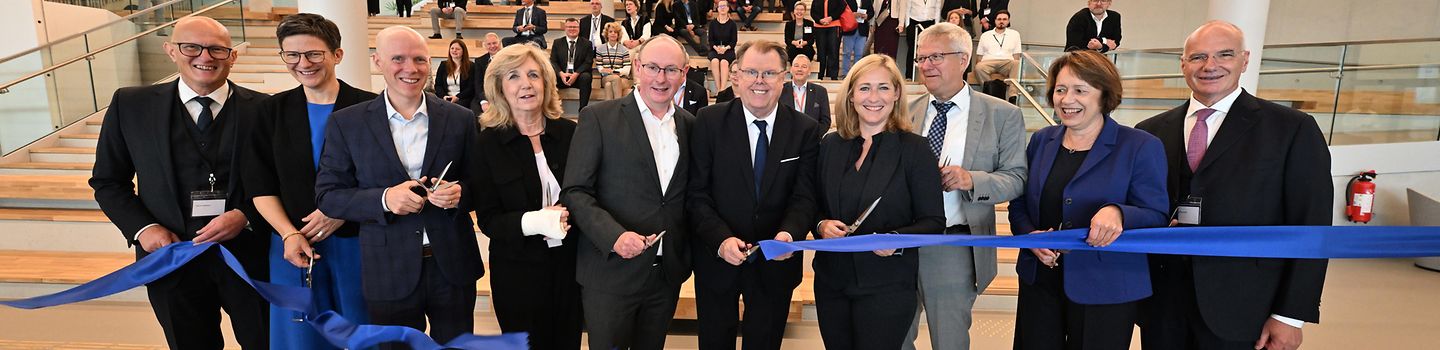 Mehrere Repräsentanten und Repräsentatinnen schneiden symbolisch ein blaues Band zur Eröffung des PREVIER durch.