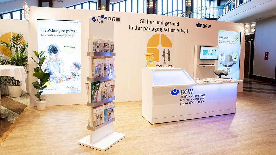 Hell beleuchteter Messestand mit Infotheke und Informationsmaterial anlässlich des BGW forum 2026 "Sicher und gesund in der Pädagogischen Arbeit"