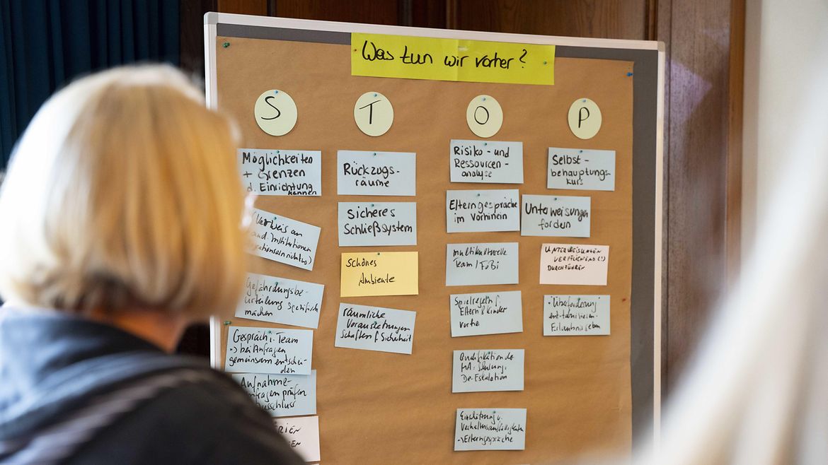 Workshop-Situation zur „STOP-Methode“ auf dem BGW forum "Sicher und gesund in der pädagogischen Arbeit“ 2026. Eine Frau blickt auf eine Metaplanwand mit angepinnten Moderationskarten, dessen Überschrift "Was tun wir vorher?" lautet. Darunter hängen Moderationskarten mit den Buchstaben "S", "T" ,"O" und "P". Unter jedem Buchstaben hängen mehrere Moderationskarten mit Einzelmaßnahmen.