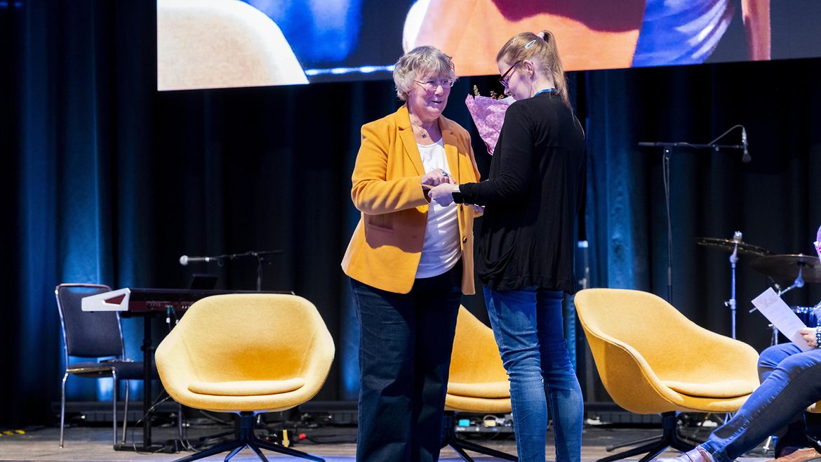 Silvia Thimm (l.) aus der BGW Selbstverwaltung mit der Gewinnerin des 2. Platzes Jaqueline Schwiderski auf einer Bühne.