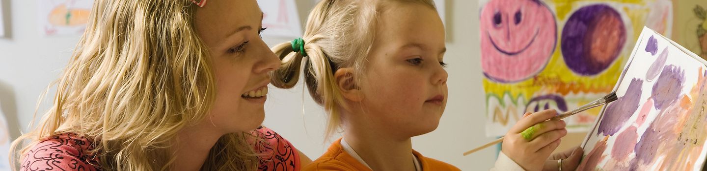 Erzieherin und Mädchen Erzieherin hilft Mädchen beim Malen