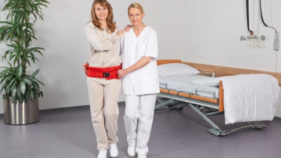 Pflegekraft macht Gehübungen mit einer Patientin, die einen Mobilisationsgürtel um die Hüfte trägt.