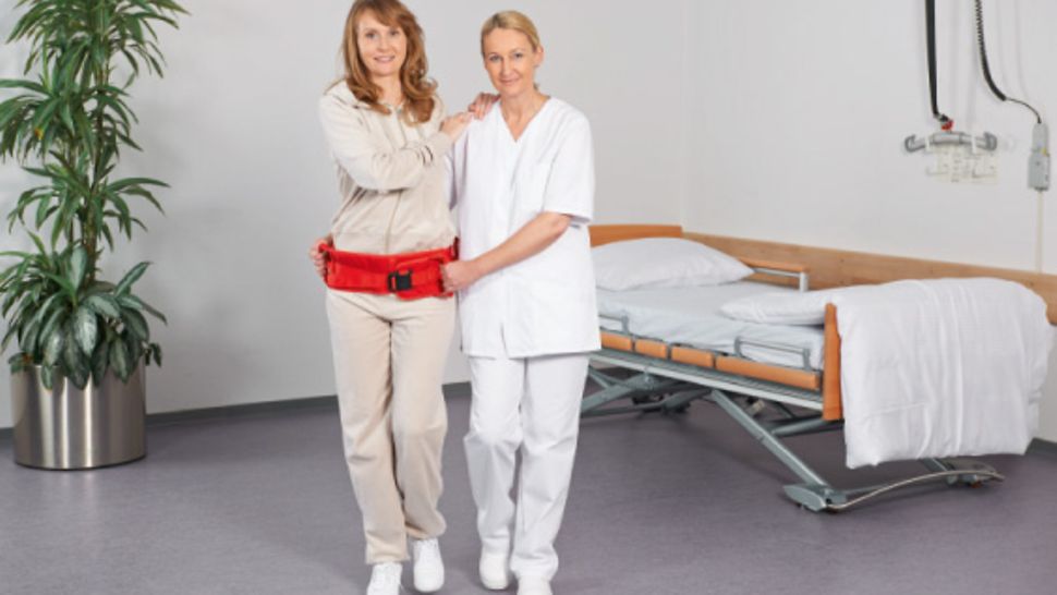 Kleine Hilfsmittel gegen Rückenbeschwerden: Mobilisationsgürtel Pflegekraft macht Gehübungen mit einer Patientin, die einen Mobilisationsgürtel um die Hüfte trägt.