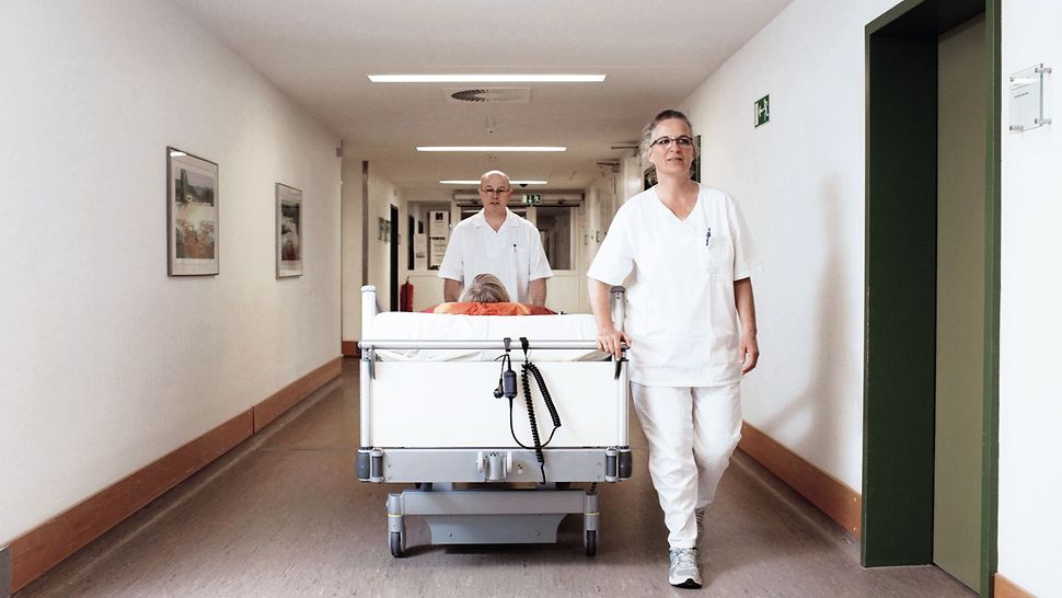 Zwei Pflegekräfte schieben ein Bett mit einer Patientin über einen Krankenhausflur