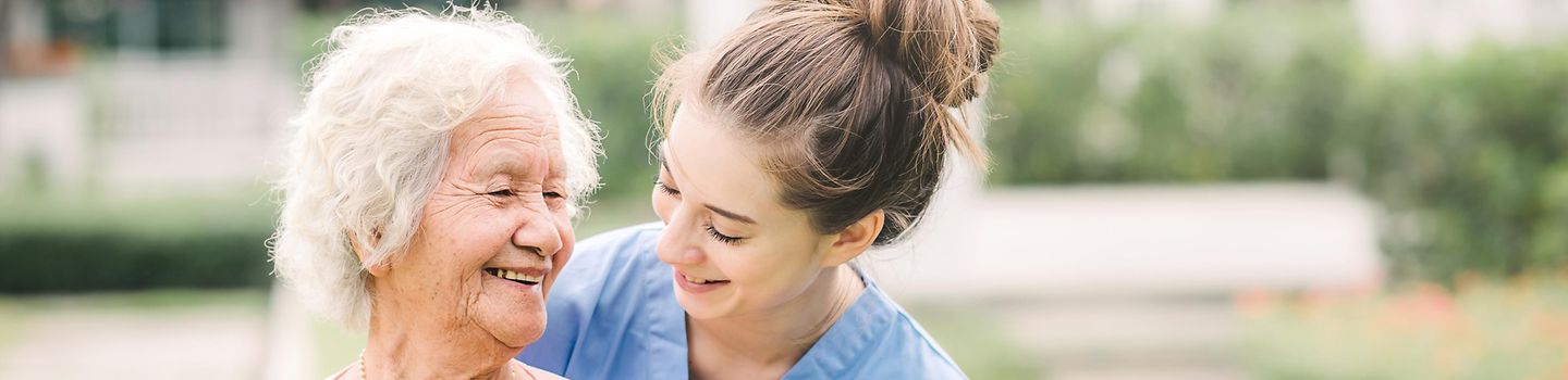 Lächelnde junge Pflegerin mit Seniorin im Freien.