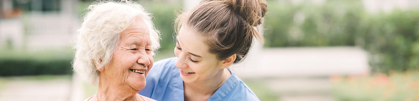 Lächelnde junge Pflegerin mit Seniorin im Freien.