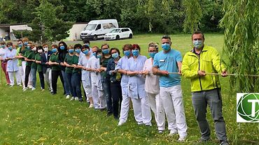 Belegschaft Tannenhof Fachpflegeheime GmbH Mitarbeitende der Tannenhofer Fachpflegeheime GmbH stehen in einer Reihe und ziehen zusammen an einem langen Seil. Alle tragen medizinische Masken.
