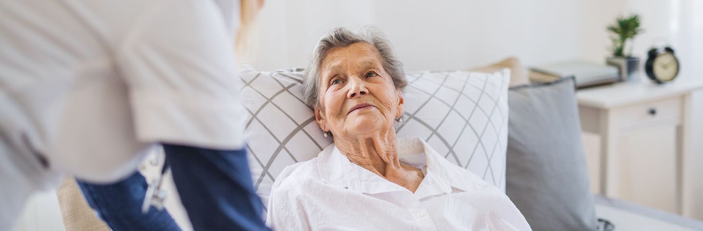 Junge Krankenschwester spricht mit einer älteren Dame, die im Bett liegt.