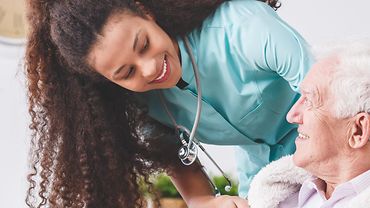 Pflegerin mit älterer Patientin Freundliche Krankenpflegerin mit einem Stehoskop deckt eine ältere Patientin mit einer Decke zu.