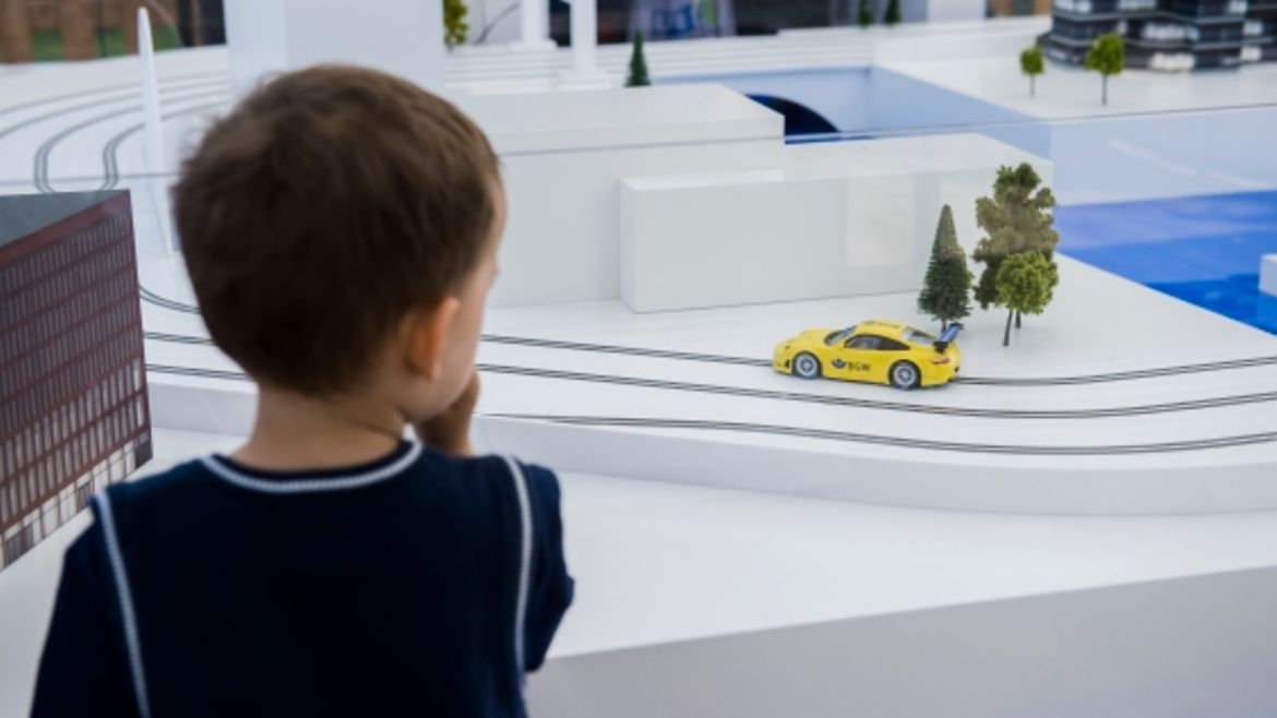 Kleiner Junge schaut sich die Carrera Bahn an, während ein gelbes Auto dort fährt.
