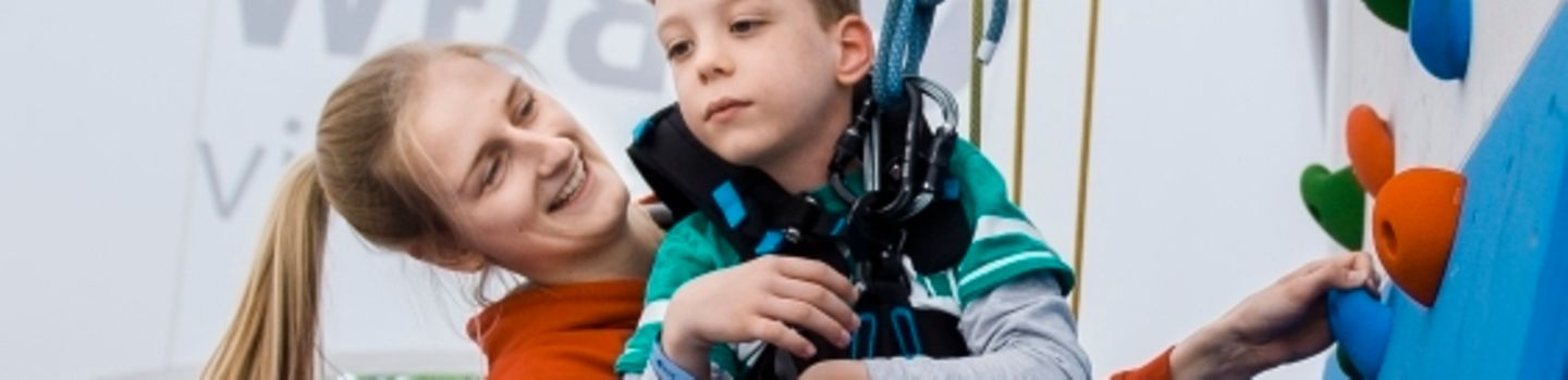 Tag der Begegnung Junge Frau hilft einem Jungen mit Handicap an der Kletterwand nach oben
