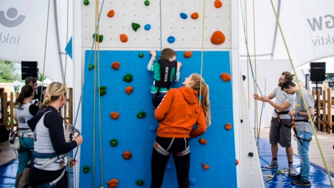 Junge Frau hilft einem Jungen mit Handicap an der Kletterwand nach oben.