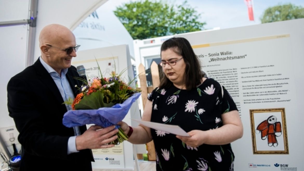 Sonia Walia hält eine Urkunde in der Hand und erhält einen Blumenstrauß vom stellvertretenden BGW-Hauptgeschäftsführer Jörg Schudmann.