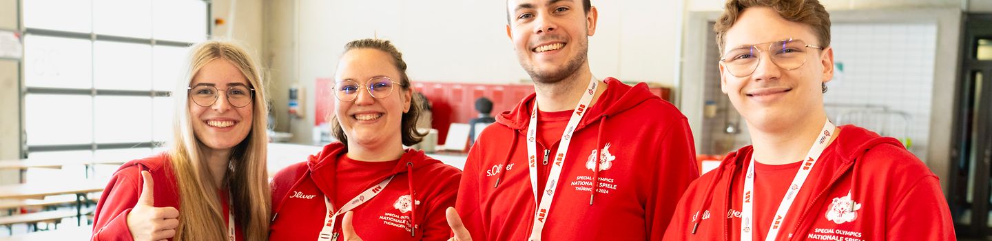 Volunteers Special Olympics Nationale Spiele 2024 Zwei Frauen und zwei Männer, alle BGW-Volunteers und mit roten Hoodies bekleidet, stehen nebeneinander und zeigen gehobenene Daumen.