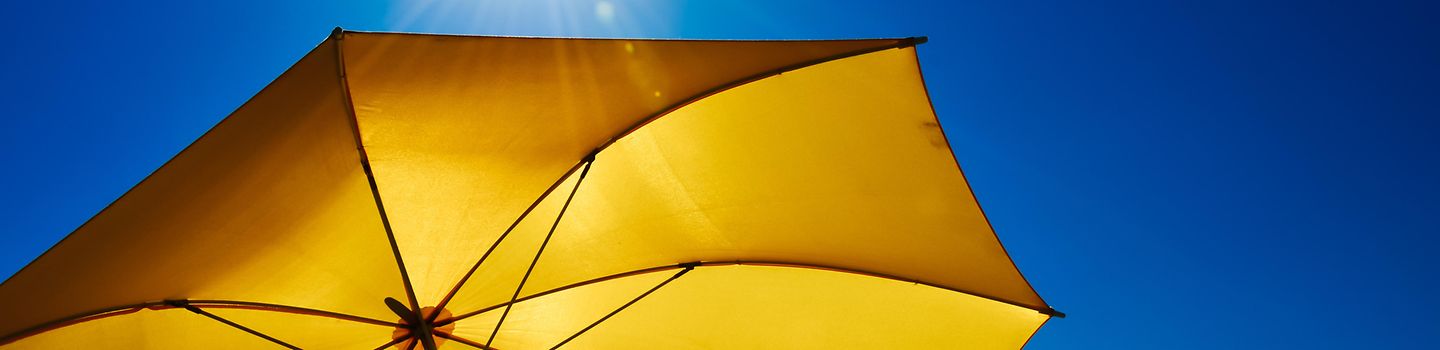 Ausstellung Kulturdimensionen Ein gelber Sonnenschirm vor blauem Himmel und darüber strahlender Sonne