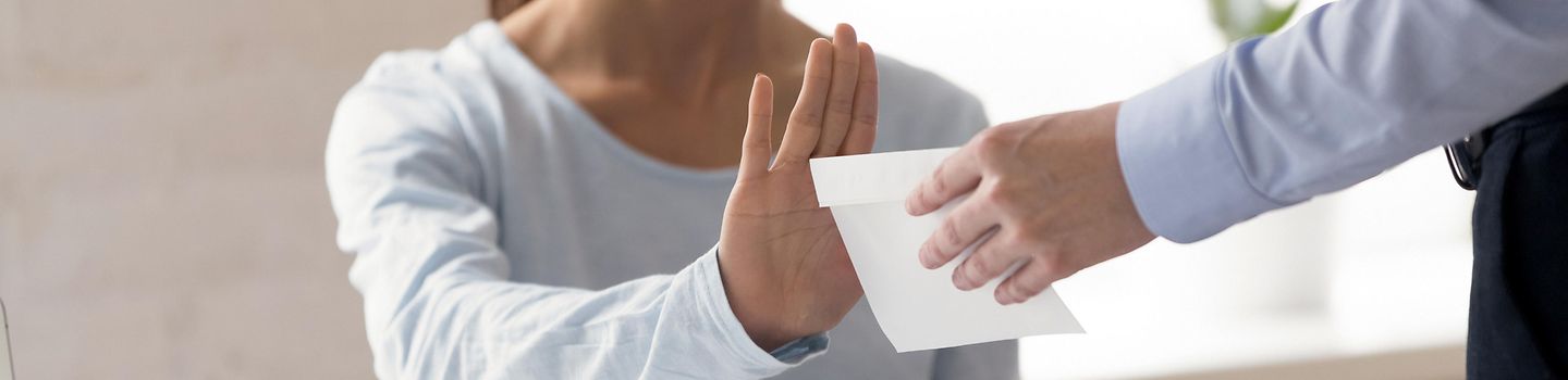 Korruptionsprävention Eine Frau hebt abwehrend die Hand, während ein Mann ihr einen Umschlag reicht.