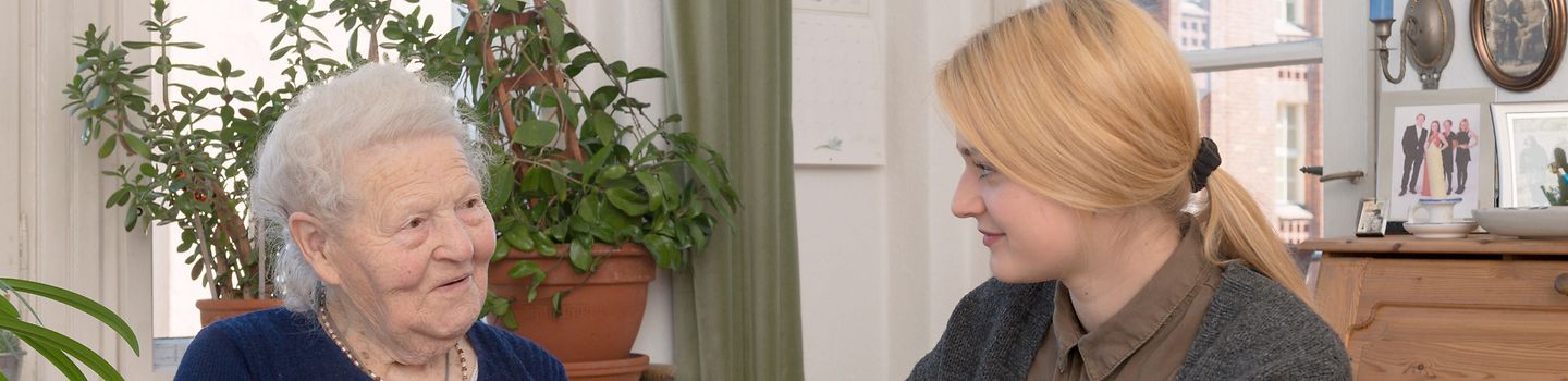 Pflege zu Hause Pflegerin unterstützt eine Seniorin beim Essen. Sie reicht ihr mundgerechte Stücke einer Orange.