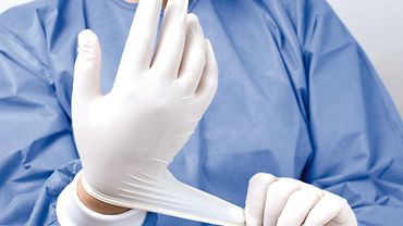 Person zieht sterilen, medizinischen Einmalhandschuh an