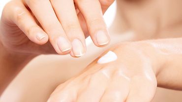Hautschutz Ein Klecks Hautcreme auf dem Handrücken einer Frau - ihre andere Hand schwebt darüber.