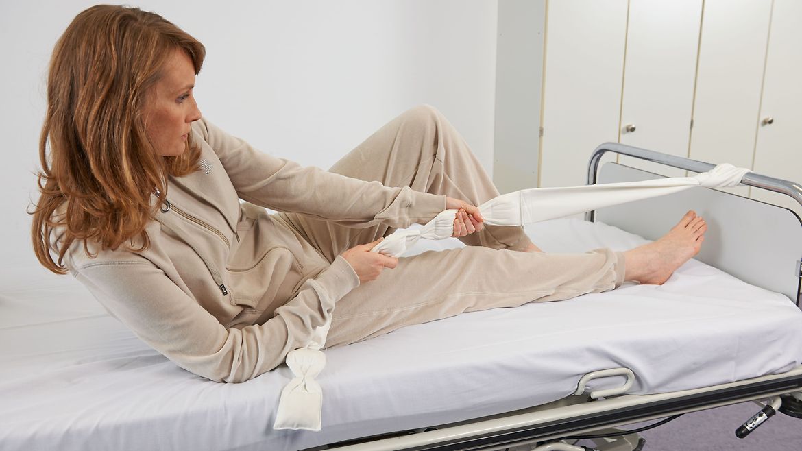 Patientin richtet sich mit dem Hilfsmittel Bettzügel im Bett auf.