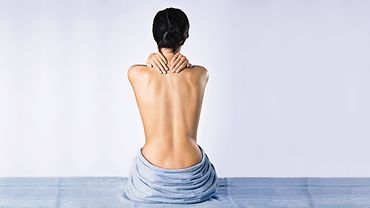 Rücken einer Frau Nackter Rücken einer Frau. Sie hält sich mit beiden Händen den Nacken.