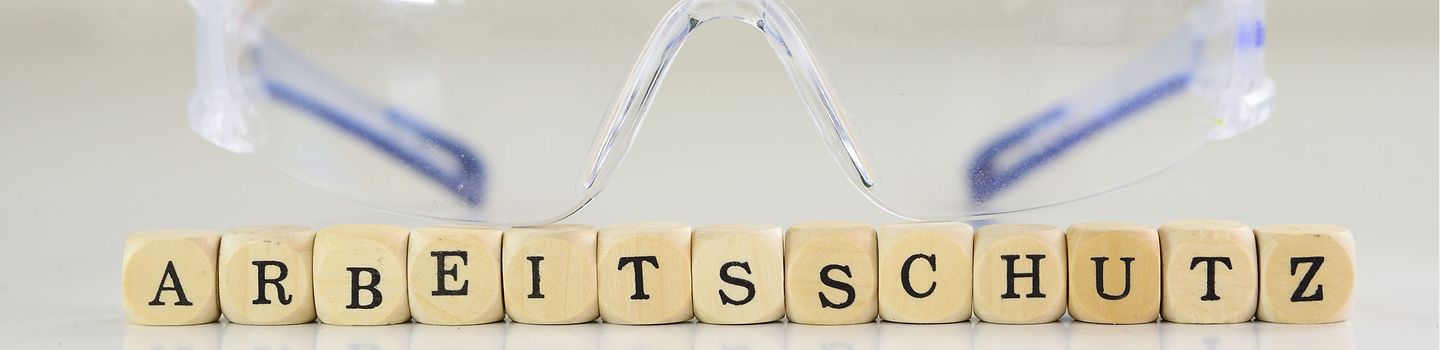 Arbeitsschutz umfasst auch den Schutz vor Infektionen. Schutzbrille und Scrabble-Buchstaben, die das Wort "Arbeitsschutz" legen