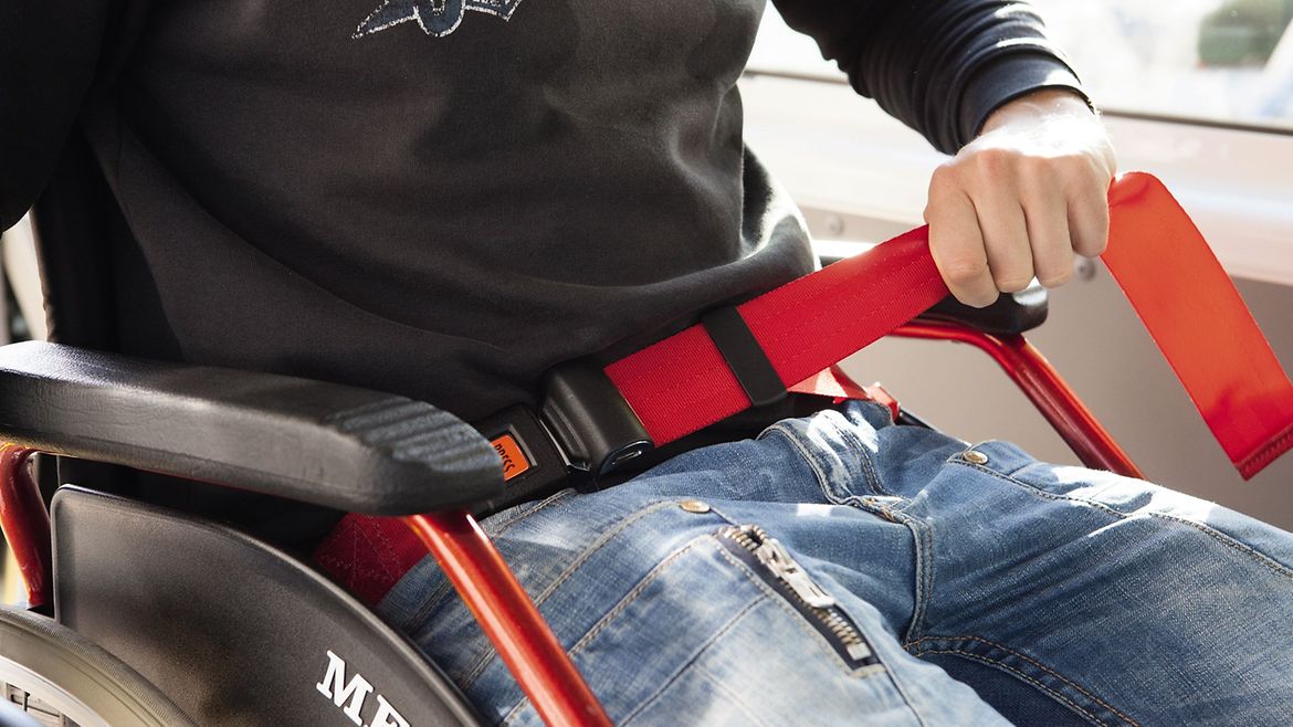 Rollstuhlnutzer spannt den Beckengurt über Längenverstellung
