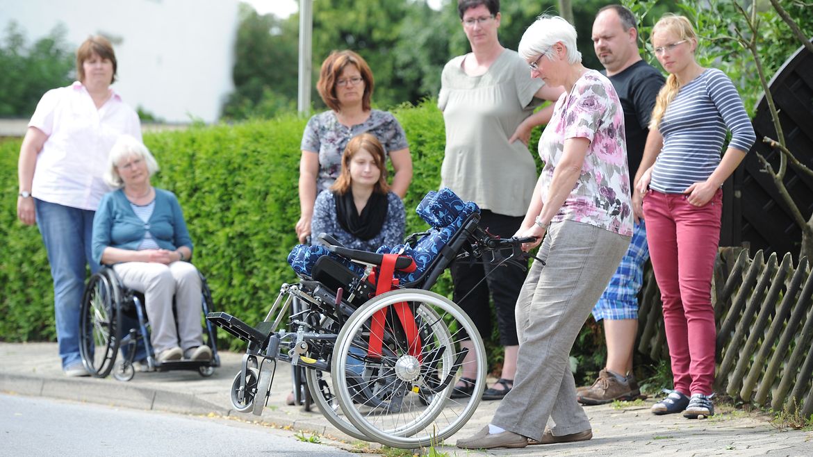Teilnehmerin hebt einen Rollstuhl rückwärts über eine Bordsteinkante.