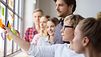 Gruppe junger Menschen arbeitet mit Post-Its an einer Wand