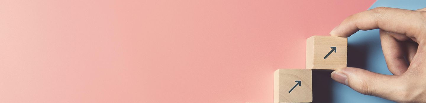 Verbesserungsprozess Hand arrangiert hölzerne Blöcke als Stufentreppe auf blauem und rosa Papierhintergrund aneinander.