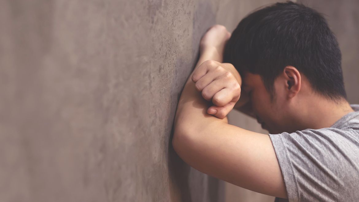 Mann lehnt sich mit den Armen vor dem Gesicht gegen eine Wand.