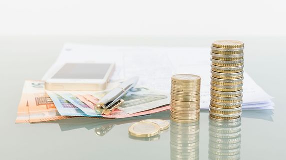 Stapel Euromünzen, Geldscheine, Stift und Handy