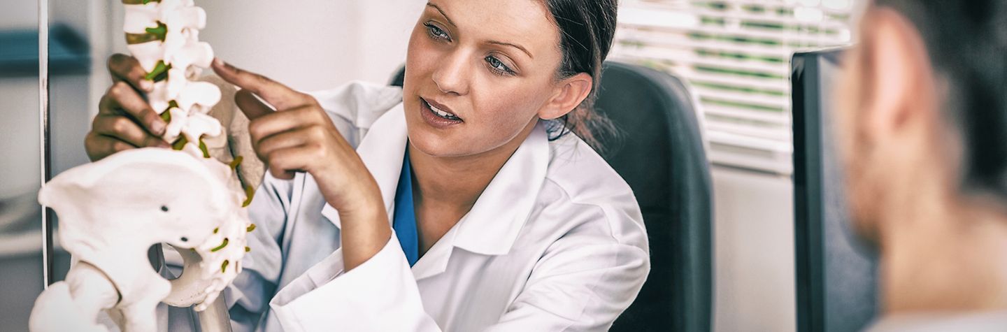 Eine Ärztin erklärt einem Patienten etwas am Modell einer Wirbelsäule.