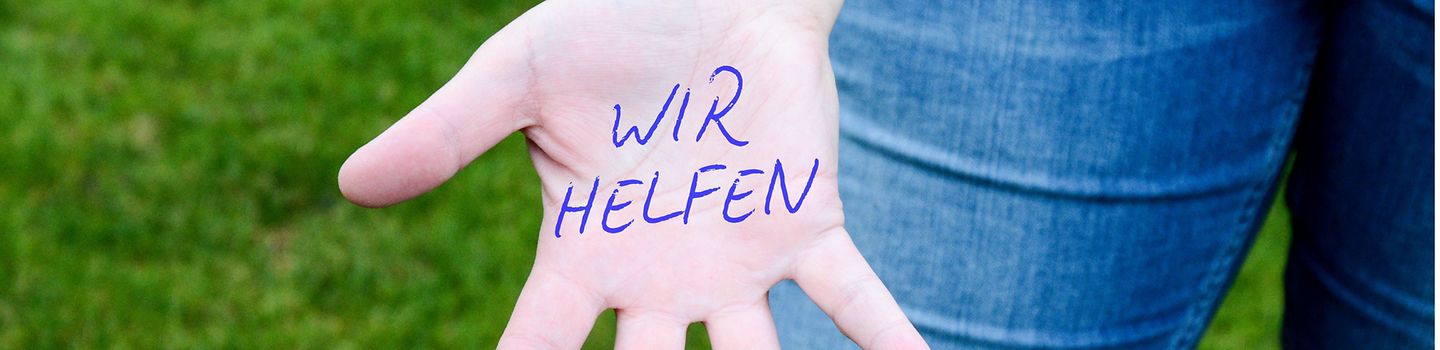 Auf einer Handinnenfläche steht "Wir helfen"