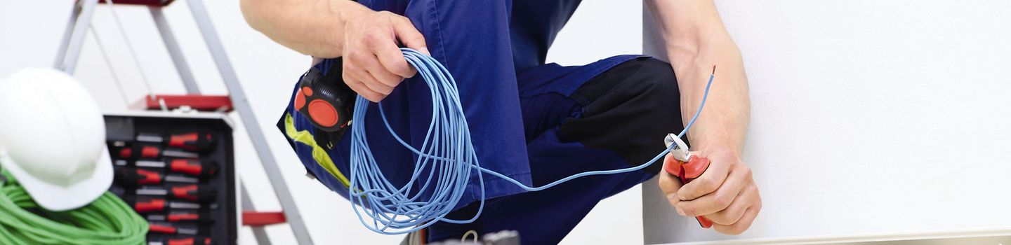 Elektriker in der Hocke sitzend mit Kabeln, Leitungen und Steckdosen
