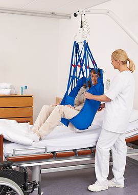Pflegerin transferiert eine Patientin mithilfe eines Wandlifters vom Bett in den Rollstuhl