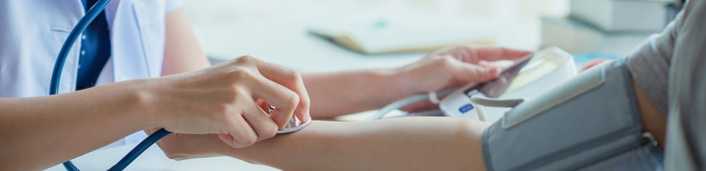 Blutdruckmessung Ärtzin misst den Blutdruck eines Patienten mit einem digitalen Messgerät und prüft den Puls mit einem Stethoskop.