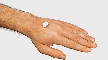 Einen etwa haselnussgroßen Klecks Creme auf dem Handrücken einer Männerhand.