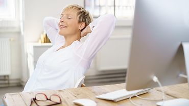 Frau am Arbeitsplatz lehnt sich entspannt zurück und schließt die Augen