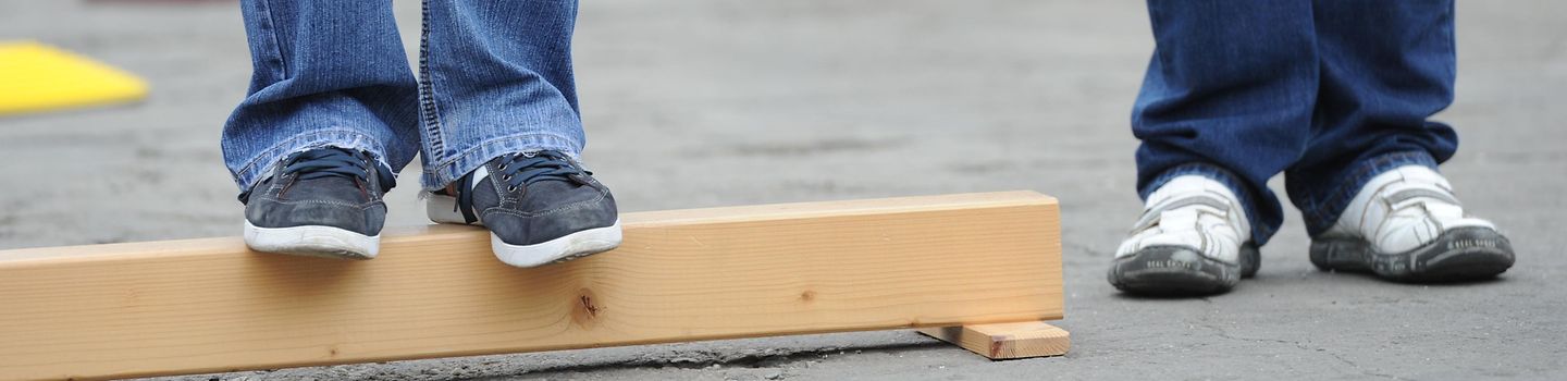 Fußgängertraining Nahaufnahme von Beinen zweier Peraonen unterhalb der Knie - eine Person steht auf einem Balken.