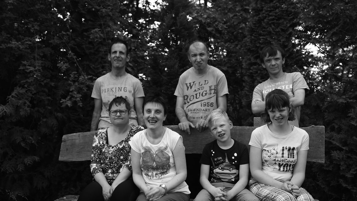 Die Künstler Mandy Kießling; Jeanine Wernicke, Lena Pietsch und Pascal Hellvoigt auf einer Holzbank sitzend; Jens Weichler, Stefan Worms und Marcel Kresse dahinter stehend.